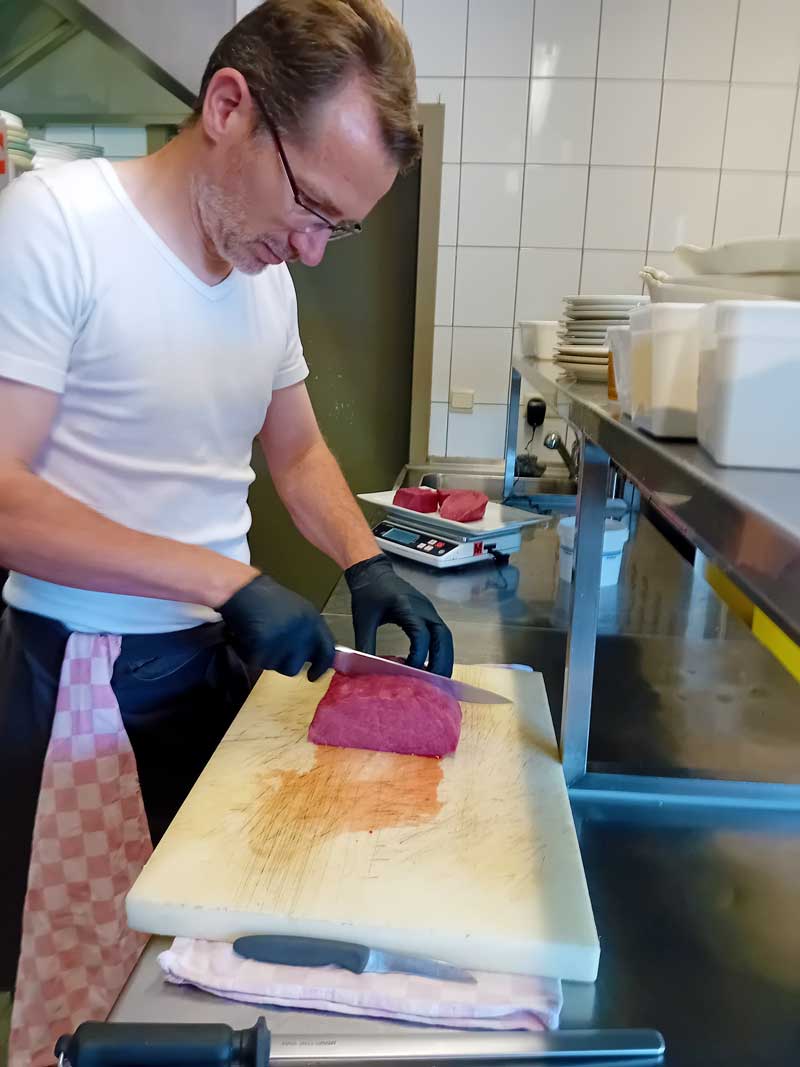 De Kok van De Poldergeus die vlees aan het snijden is in de keuken